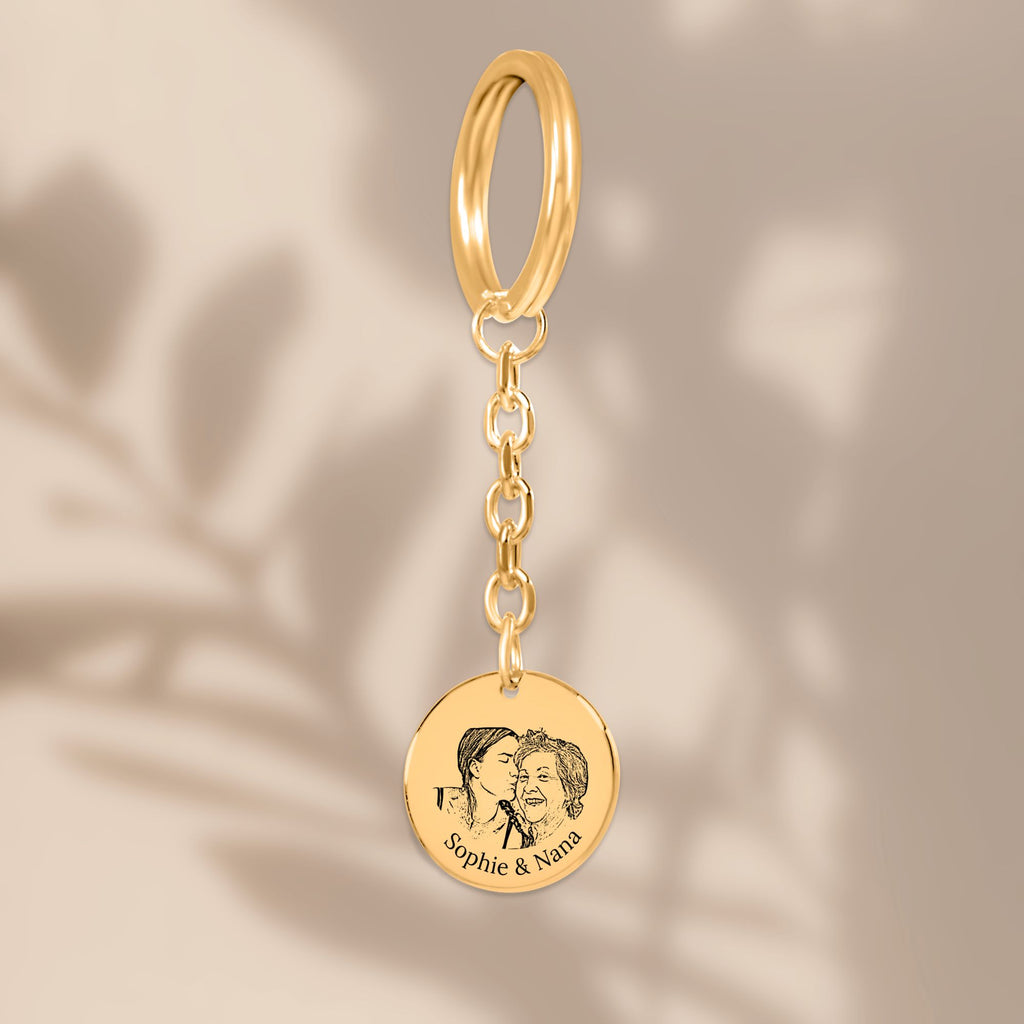 De gouden muntsleutelhanger met lijnportret, hangend tegen een beige achtergrond