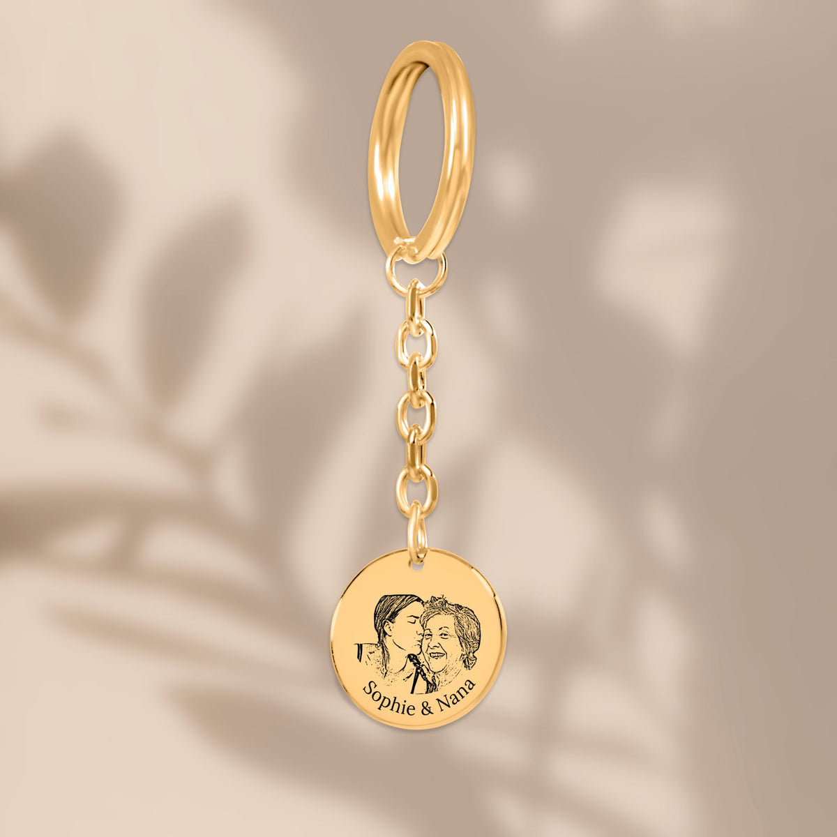 De gouden muntsleutelhanger met lijnportret, hangend tegen een beige achtergrond