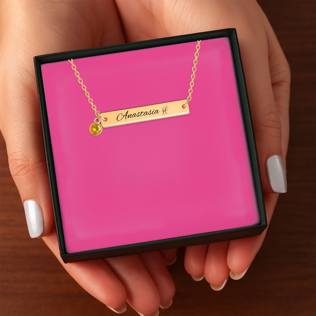 Het geschenkdoosje met de gouden horizontale staafketting met geboortesteen, in twee handen