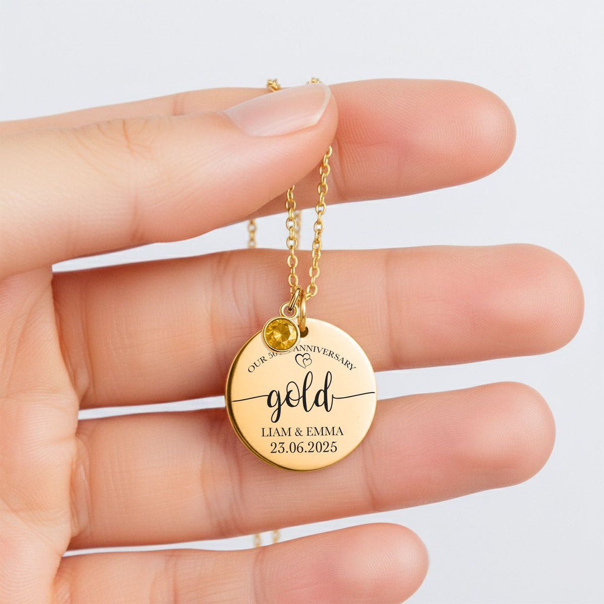 De gouden muntketting met geboortesteen, in de vingers gehouden