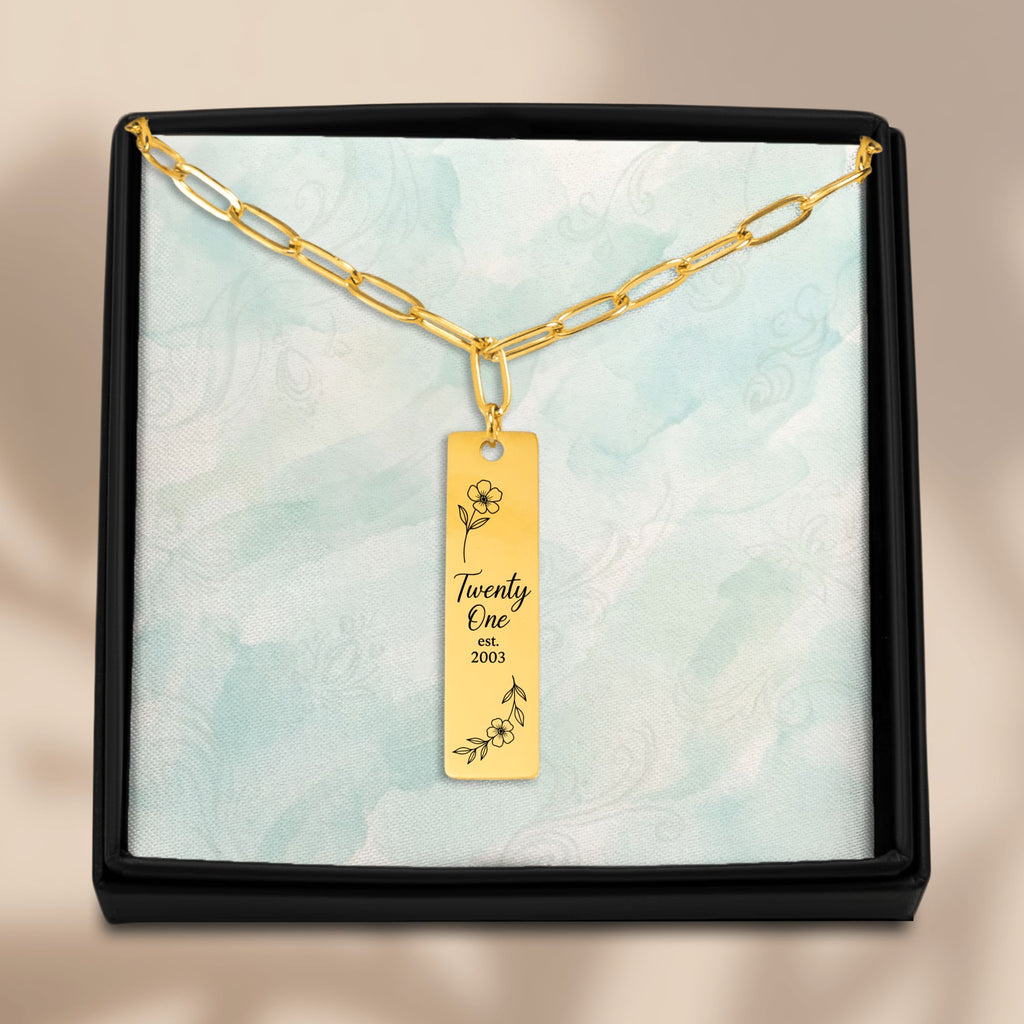 De gouden paperclipketting met gegraveerde staaf in het geschenkdoosje, van bovenaf