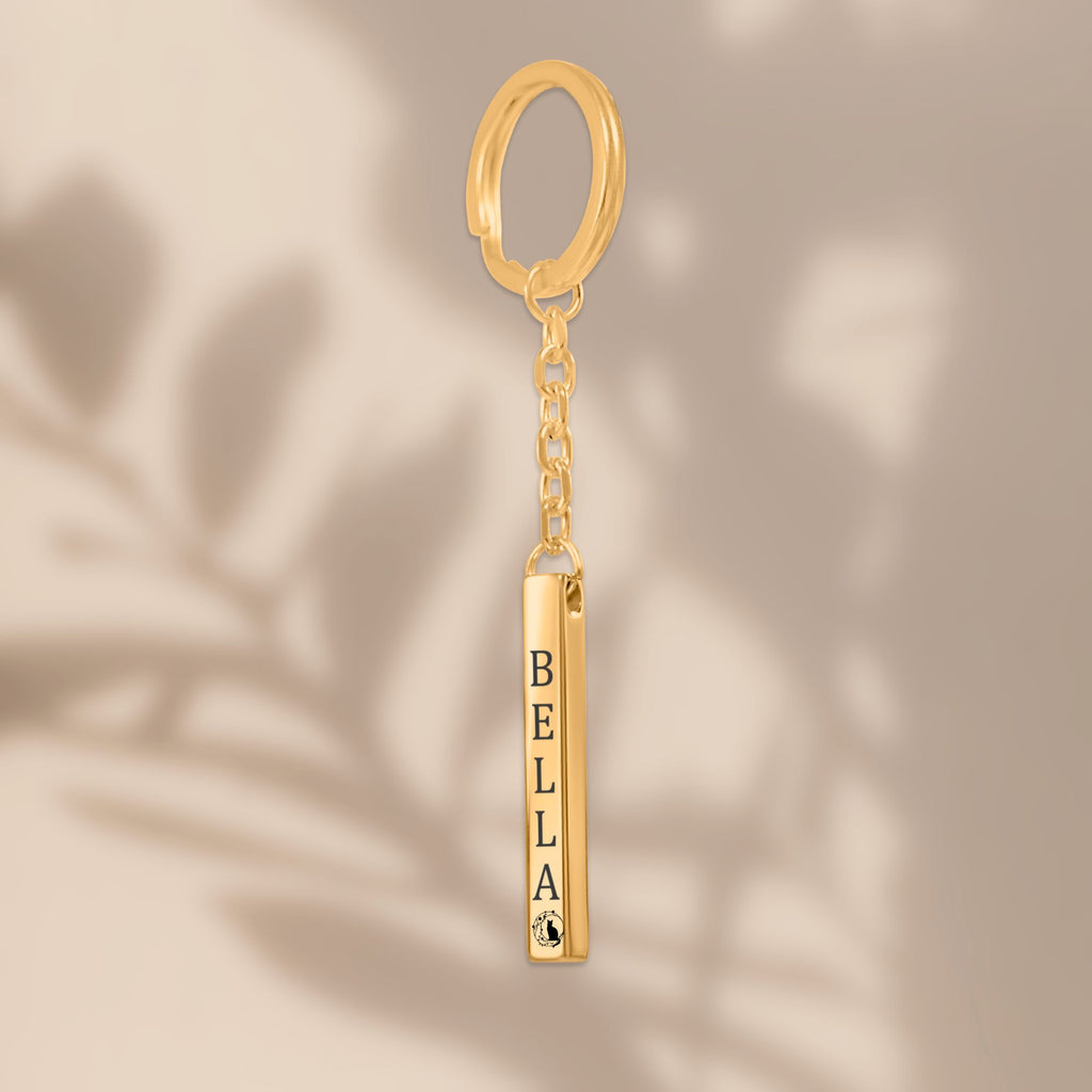 De gouden 3D-staafsleutelhanger, hangend tegen een beige achtergrond