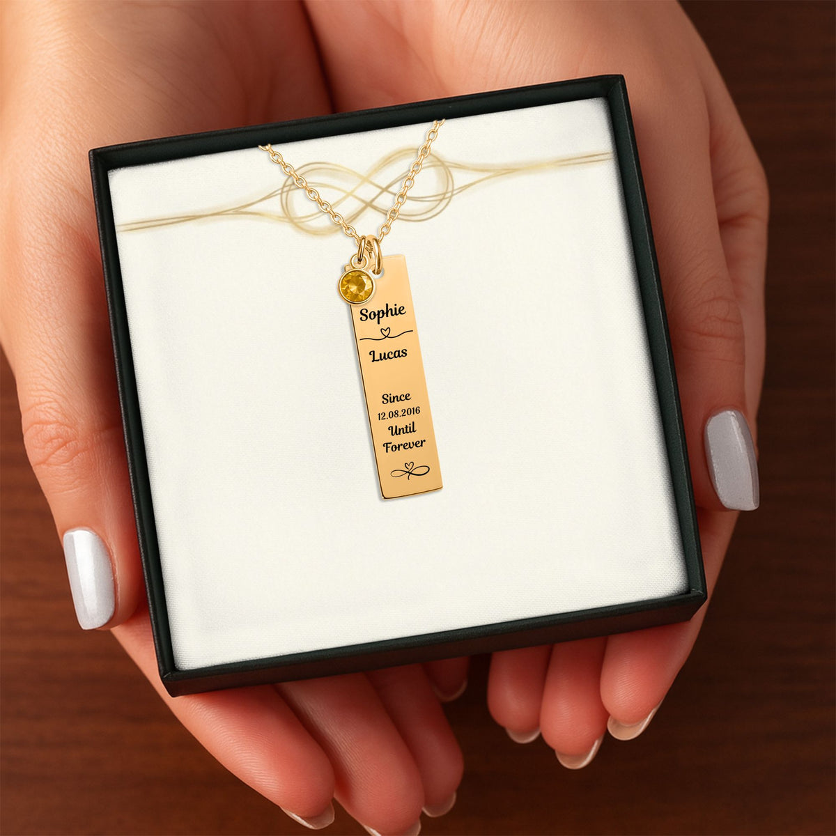Het geschenkdoosje met de gouden staafketting met geboortesteen, in twee handen