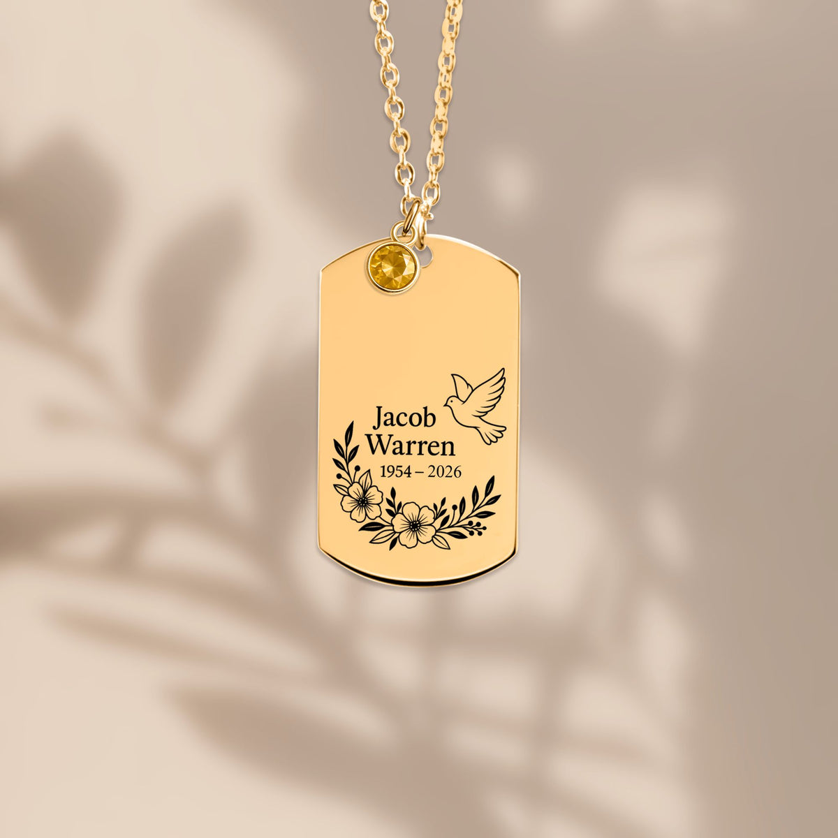De gouden ketting met gegraveerd plaatje, liggend tegen een lichte achtergrond
