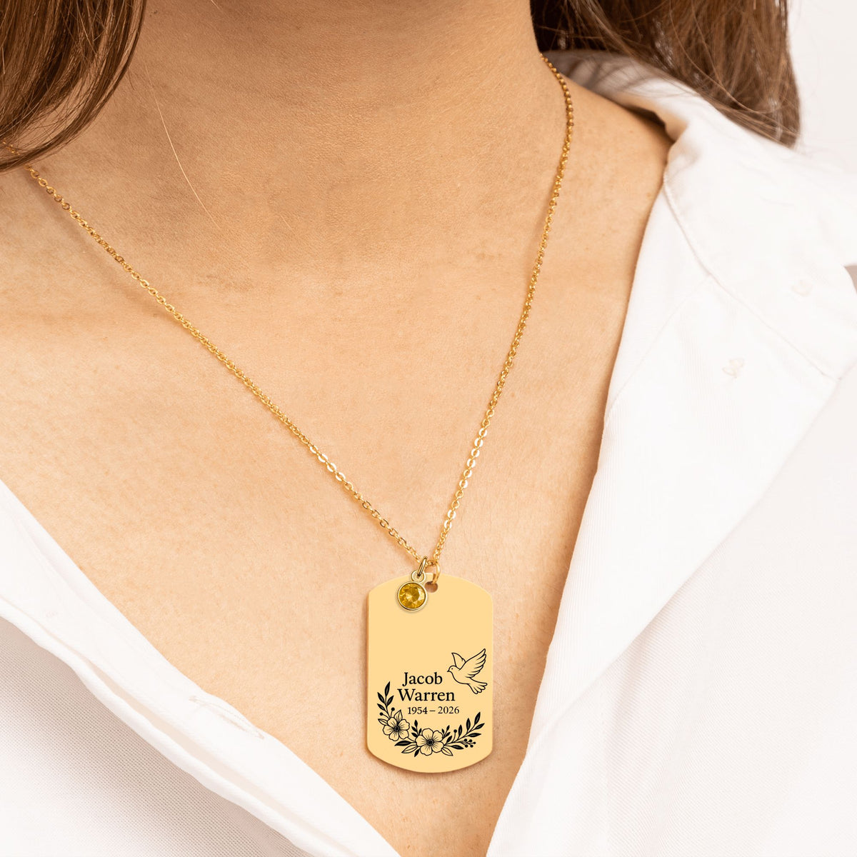 De gouden ketting met gegraveerd plaatje met geboortesteen om de hals gedragen