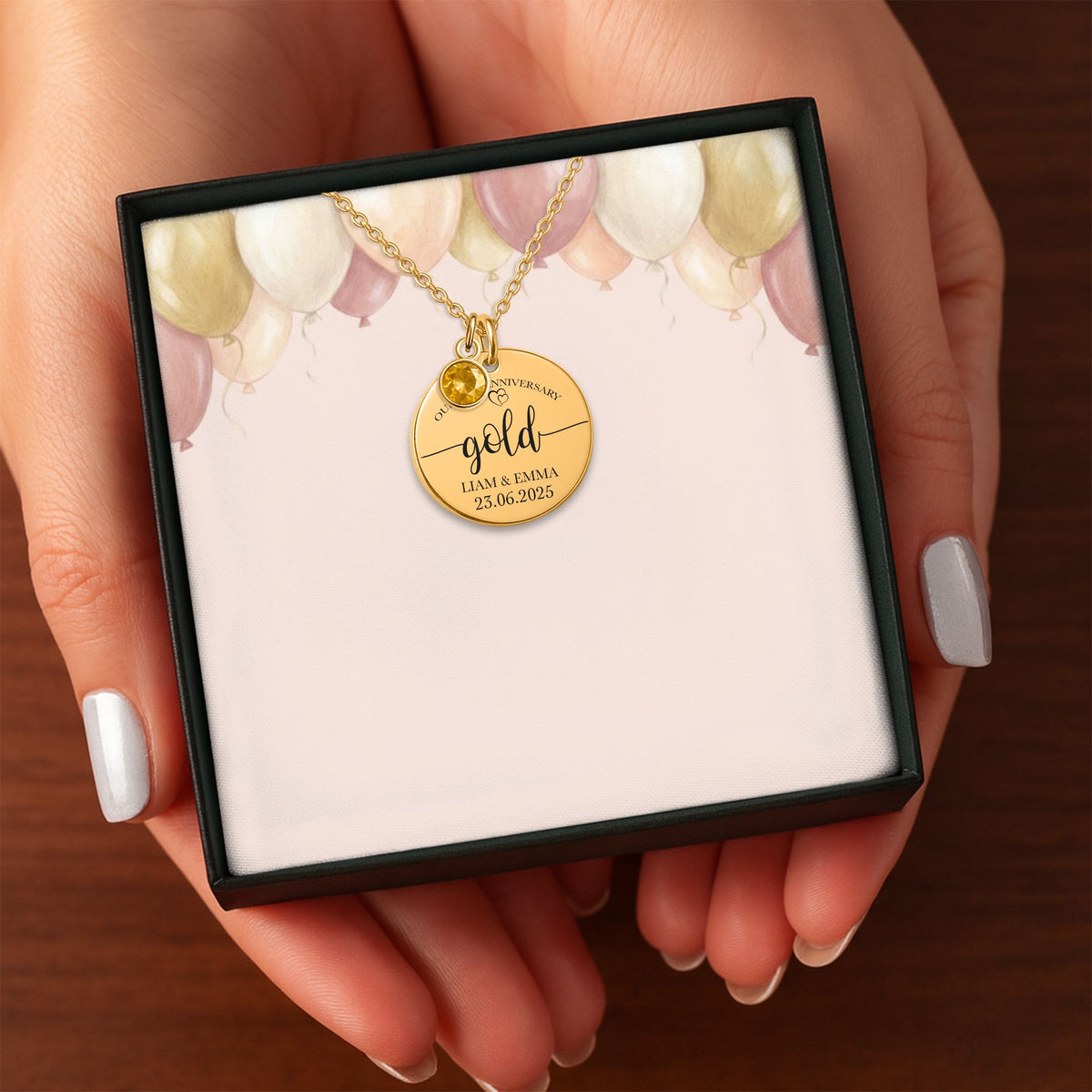 Het geschenkdoosje met de gouden muntketting met geboortesteen, in twee handen