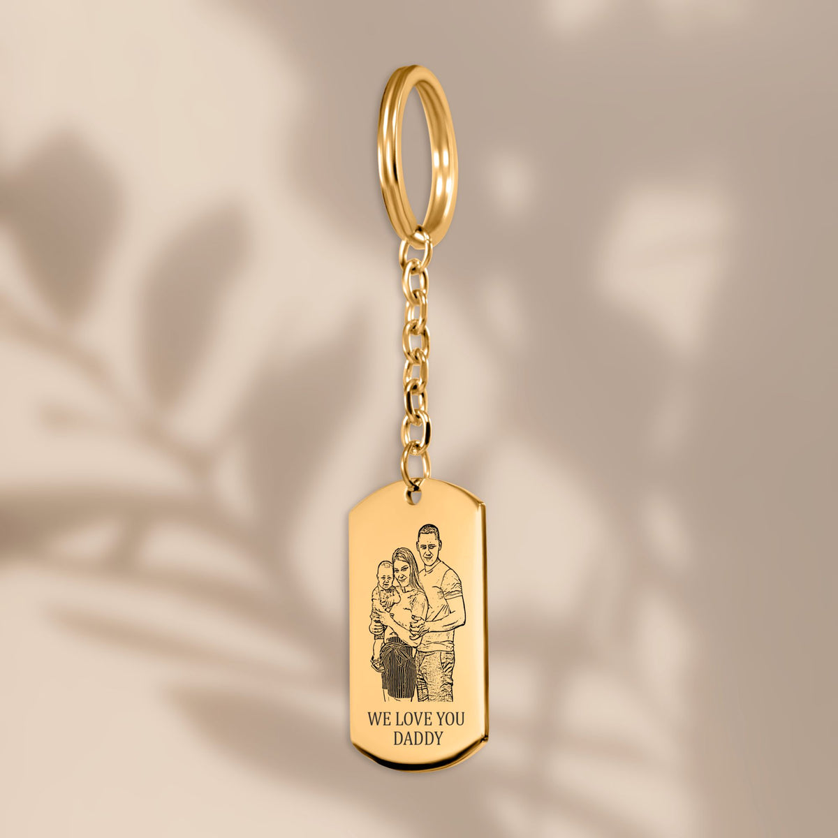 De gouden sleutelhanger met gegraveerd plaatje, hangend tegen een beige achtergrond